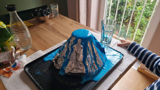 Kind führt Vulkan Experiment mit blauer Lava durch. Naturmacher Vulkan Experiment für Kinder. Anleitung zum Download verfü...