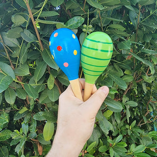 Hand hält zwei bunte Holz-Babyrasseln (Maracas) von Relaxday, blau mit Punkten und grün gestreift.