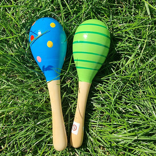 Zwei bunte Holz-Babyrasseln (Maracas) von Relaxday auf grünem Gras. Blau mit Punkten und grün gestreift.