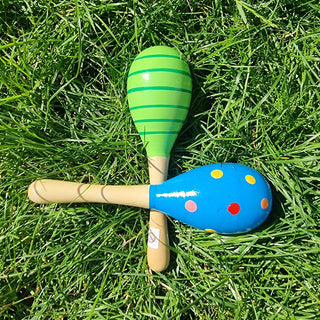 Zwei bunte Holz-Babyrasseln (Maracas) von Relaxday auf grünem Gras. Eine grün gestreift, die andere blau mit bunten Punkte...