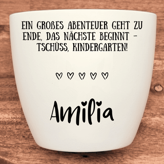 Weißer Blumentopf mit Gravur "Ein großes Abenteuer geht zu Ende, das nächste beginnt - Tschüss, Kindergarten!" und dem Nam...