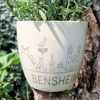 Keramiktopf mit Bensheim-Motiv und Pflanzen, von Naturmacher, auf einem Baumstamm im Freien.