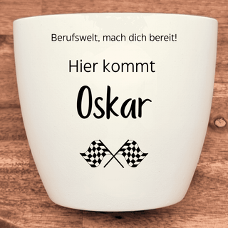 Weißer Blumentopf mit Aufschrift "Berufswelt, mach dich bereit! Hier kommt Oskar" und Rennflaggen. Abschlussgeschenk von N...