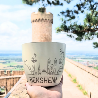 Hand hält Bensheim-Topf von Natur Macher, mit Skyline-Design, vor Burghintergrund.