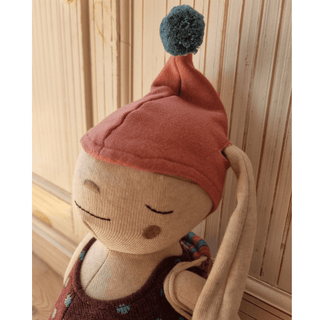 Kuschelhase Alva von ava&yves mit rosafarbener Mütze und blauem Bommel, beigefarbenem Körper und braunem Kleidchen. Spielz...