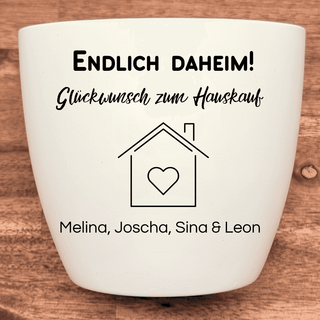 Weißer Blumentopf mit "Endlich Daheim!", Haus-Symbol und Personalisierung als Einzugsgeschenk.