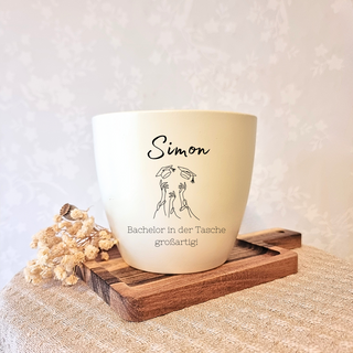 Beiger Blumentopf mit "Simon", geworfenen Bachelorhüten und "Bachelor in der Tasche, großartig!" graviert. Abschlussgesche...