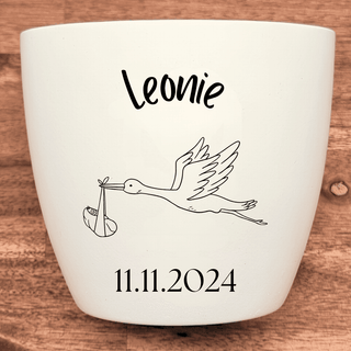 Weißer Blumentopf mit Storch, Baby und Aufschrift "Leonie 11.11.2024". Geburtsgeschenk.
