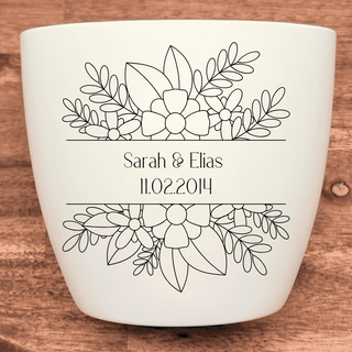 Weißer Blumentopf mit gravierten Blumen und dem Text "Sarah & Elias 11.02.2014". Hochzeitsgeschenk von Natur Macher.