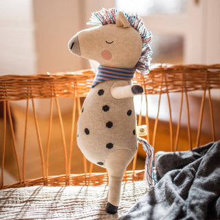 Kuscheltier Rainbow Horse von ava&yves aus Bio-Strick, grau mit schwarzen Punkten und buntem Schal. Stehend dargestellt.